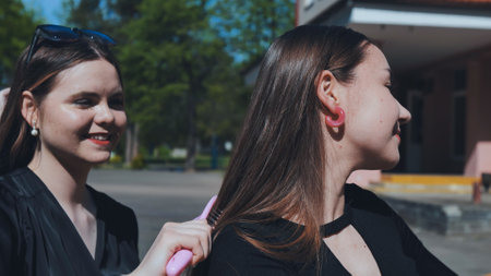 Two teenage girls bonding after school, one carefully brushing the others hair with a pink brush on a sunny dayの写真素材
