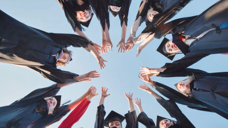 Students in graduation attire raising hands in the air to form a circle in the sky, celebrating their graduation dayの写真素材