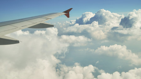Airplane wing gliding over soft, white clouds, revealing expansive blue sky background and evoking freedom of high altitude travelの写真素材