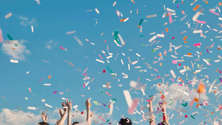 High school graduates joyfully tossing vibrant confetti in the air against a clear blue skyの写真素材