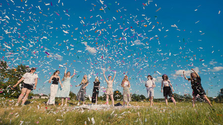 High school graduates celebrate with colorful confetti on a sunny summer dayの写真素材