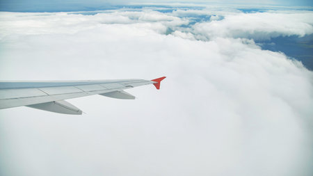 Airplane wing gliding above fluffy clouds, revealing expansive landscape stretching beneathの写真素材