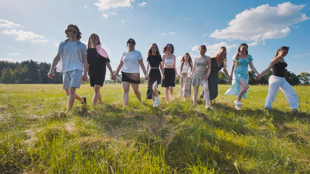 High school students happily holding hands and strolling through a sunny field during the summerの写真素材
