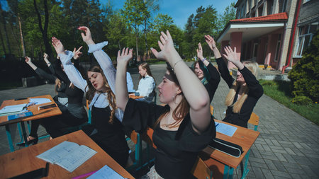 Female students taking a break and stretching their arms at outdoor desks during school dayの写真素材