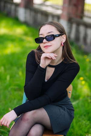 Stylish high school student relaxing during her break, seated in the schoolyard with sunglasses and a contemplative lookの写真素材