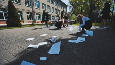 Female students cleaning up papers in the schoolyard on the last day of schoolの写真素材