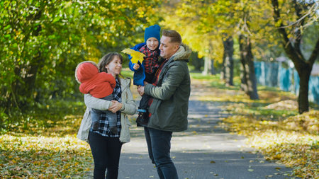 Loving parents hugging children, walking amid colorful autumn foliage, basking in golden sunlight filtering through treesの写真素材