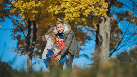 Cheerful family gathering beneath golden autumn foliage, laughing and playing together during crisp seasonal afternoonの写真素材
