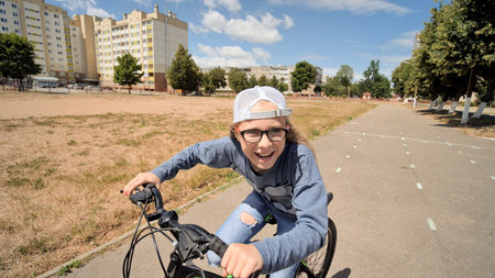 Happy school girl riding bicycle in a city park during sunny summer day, smiling and having fun