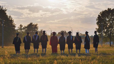 Graduates in academic attire and caps standing in a field at sunset following their graduation