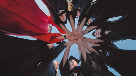 Smiling graduates join hands in unity, forming a circle to celebrate their academic success and...