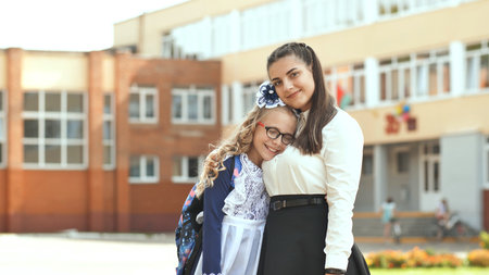 Schoolyard sisters hugging tightly, smiling with genuine affection and shared excitement during bright midday momentの写真素材