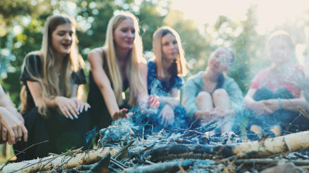 School friends warming up around a bonfire in summer camp, enjoying their vacation togetherの写真素材