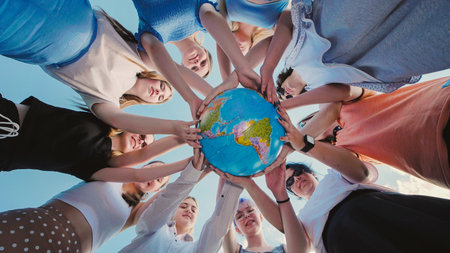 Group of school friends holding a globe, symbolizing global unity and care for the environment, promoting sustainability and responsibility towards earthの写真素材