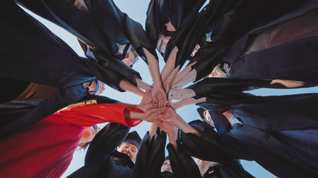 Group of graduates in academic gowns holding hands in a circle, representing unity and achievement