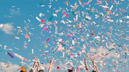 High school graduates joyfully tossing colorful confetti into the air against a backdrop of clear blue skyの写真素材