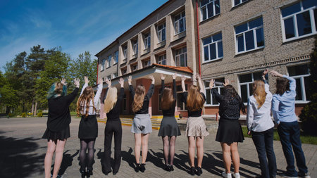 Group of happy students waving goodbye to their school on the last day, celebrating graduation and...