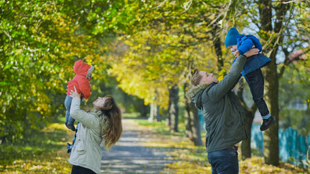 Parents lifting their two young children in a beautiful autumn park, enjoying a sunny day together
