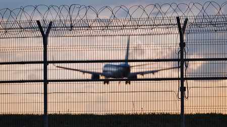 Airplane landing behind barbed wire fence at sunsetの写真素材