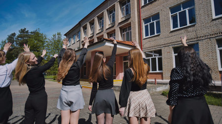 Group of happy female students waving goodbye to school on their last school day, celebrating the end of the academic yearの写真素材