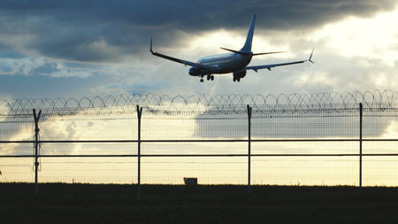 Airplane landing at airport with security fence at sunset, travel conceptの写真素材