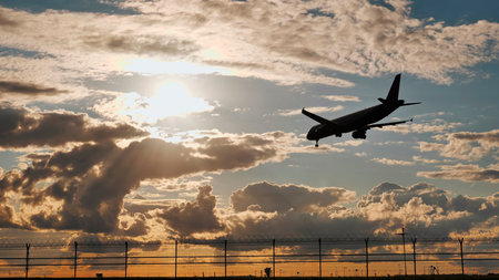 Passenger airplane landing at sunset over airport fence
