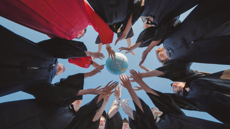 Graduates in academic gowns reaching for a globe, representing their global ambitions and unity in a diverse worldの写真素材