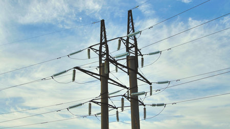 Electricity pylons rising against a backdrop of a cloudy sky, supporting essential power lines for...