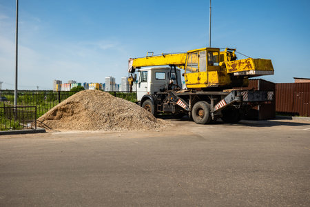 Crane truck on construction site next to a gravel pile and city buildings