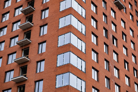 Modern building facade featuring red brick, many windows, and concrete balconies