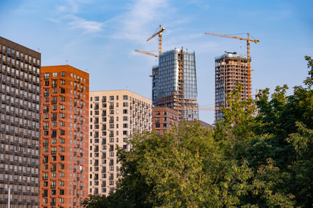 Urban cityscape with new residential towers rising above buildings, cranes on a blue sky