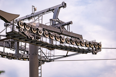 Metal ski lift tower and wheels supporting heavy cables against a clear skyの写真素材