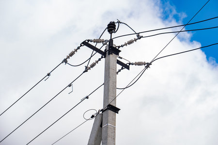 Utility pole carrying power lines with ceramic insulators against cloudy sky