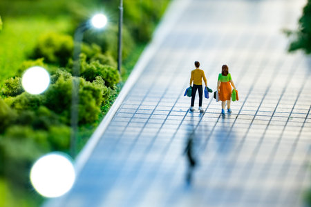 Miniature couple walking on sidewalk after shopping, carrying bagsの写真素材