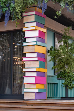 Giant stacked colorful books forming a whimsical pillar sculpture at an outdoor cafeの写真素材