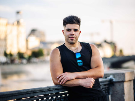 Young man posing confidently on city embankment with sunglasses in urban scene