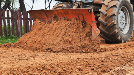 Tractor earthmoving, leveling red soil on construction site, moving dirt