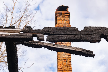 Charred wooden remains and brick chimney standing after house fire disaster