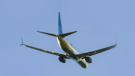 Commercial passenger jet airplane taking off, ascending into a clear blue sky. Low angle view from...