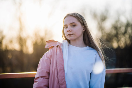Young girl looking at camera during golden hour, long hair flowing in the windの写真素材