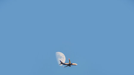 An airplane takes off against the moon and blue sky.