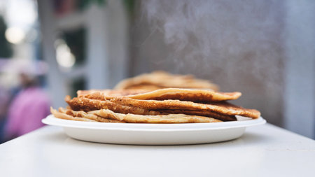 Stack of hot pancakes with steam rising on a white plate outdoorsの写真素材