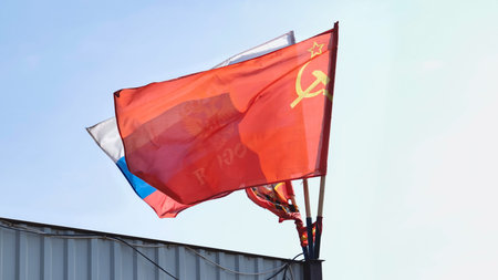Soviet and Russian flags waving in the wind over a metallic fence