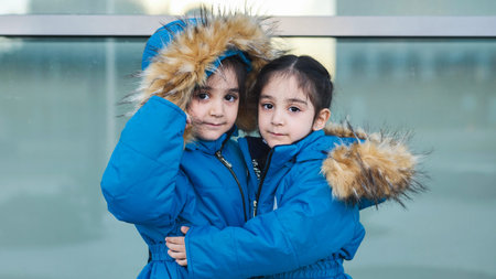 Adorable identical twin girls wearing warm blue winter parkas and huggingの写真素材