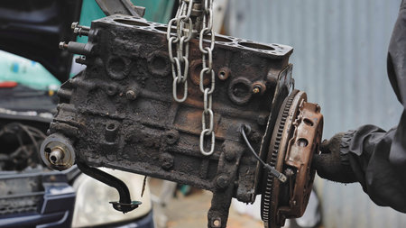 Mechanic lifting greasy car engine block for repair and maintenance in garage