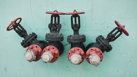 Four industrial valves with red wheels on a teal wall for fluid control