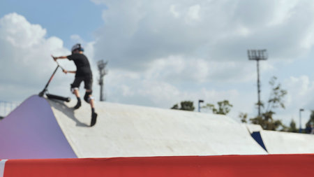 Young person riding scooter at skate park, performing extreme jump on ramp