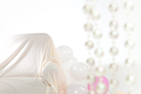 Interior with white and pink balloons and sofa. On the right blurry transparent pearls.