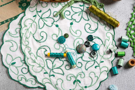 Silk green thread in needle, on work table. With spools of thread, buttons, embroidery fabrics. Horizontal.の写真素材