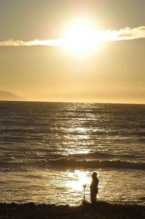 Man with tripod on beach in sunsetの写真素材